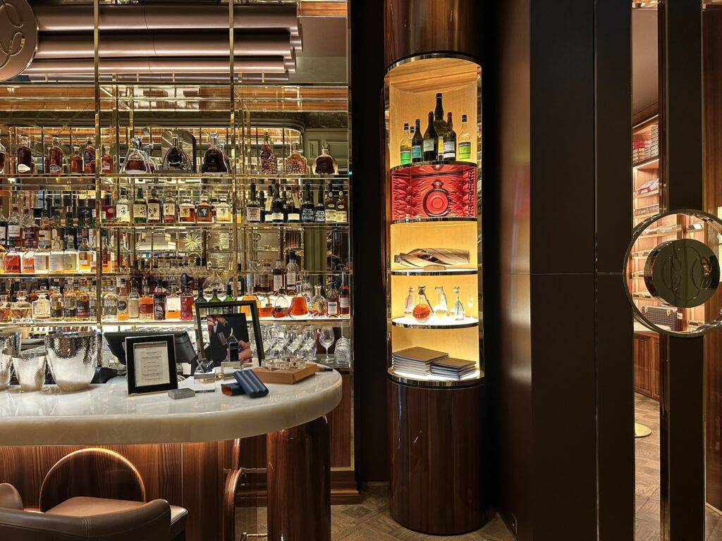Luxurious bar interior with illuminated bottles on glass shelves and dark wood panels behind a curved marble counter.